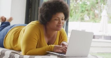 Yerde yatan ve dizüstü bilgisayar kullanan mutlu ve boyut olarak Afrikalı Amerikalı bir kadının videosu. Yaşam tarzı, rahatlık, evde teknolojiyle vakit geçirmek..