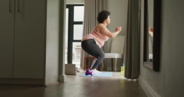 Büyük boy Afro-Amerikan kadının evde egzersiz yaptığı, çömeldiği bir video. aktif sağlıklı yaşam tarzı, evde egzersiz.