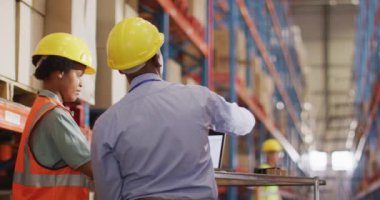 Afrika kökenli Amerikalı erkek ve kadın işçiler kask takıyor ve depoda dizüstü bilgisayar kullanıyorlar. küresel iş, nakliyat ve teslimat.