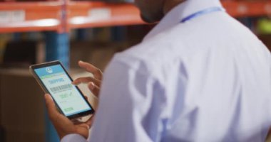 Depoda akıllı telefon kullanan kasklı Afrikalı Amerikalı erkek işçi. küresel iş, nakliyat ve teslimat.