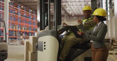 Afrika kökenli Amerikalı erkek ve kadın işçiler güvenlik kıyafetleri giyip depoda konuşuyorlar. küresel iş, nakliyat ve teslimat.