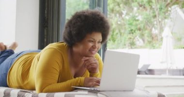 Yerde yatan ve dizüstü bilgisayar kullanan mutlu ve boyut olarak Afrikalı Amerikalı bir kadının videosu. Yaşam tarzı, rahatlık, evde teknolojiyle vakit geçirmek..