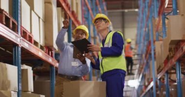 Çeşitli erkek işçiler güvenlik kıyafetleri giyip depoda konuşuyorlar. küresel iş, nakliyat ve teslimat.