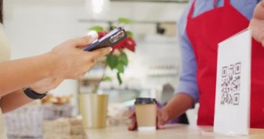 Çift ırklı bir kadının akıllı telefonlu QR kodunu taramasının videosu. Kahve ve fil dükkanı, küçük bağımsız işler yürütüyor..