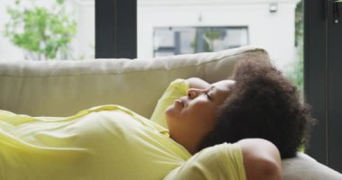 Kanepede dinlenen Afrikalı Afrikalı Amerikalı bir kadının videosu. Yaşam tarzı, boş zaman, evde boş zaman geçirme..