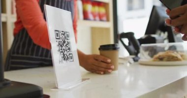 Video of hands of biracial man scanning qr code with smartphone. coffee and bistro shop, running small independent business.