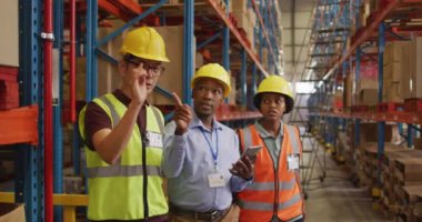 Çeşitli erkek ve kadın işçiler güvenlik kıyafetleri giyip depoda konuşuyorlar. küresel iş, nakliyat ve teslimat.