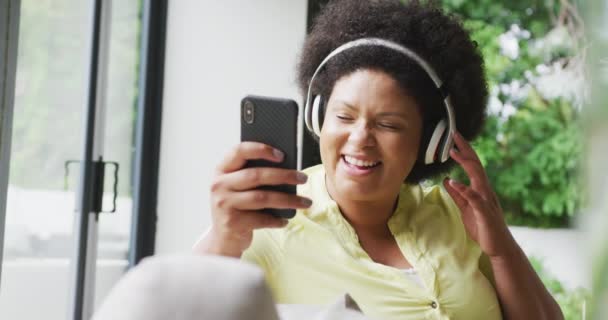 Видео Счастливой Плюс Размер Африканской Женщины Наушниками Диване Слушающей Музыку — стоковое видео