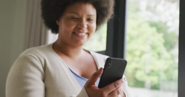 スマートフォンを使ってアフリカ系アメリカ人女性の幸せと大きさの動画 ライフスタイルレジャーテクノロジーで家で自由時間を過ごし — ストック動画