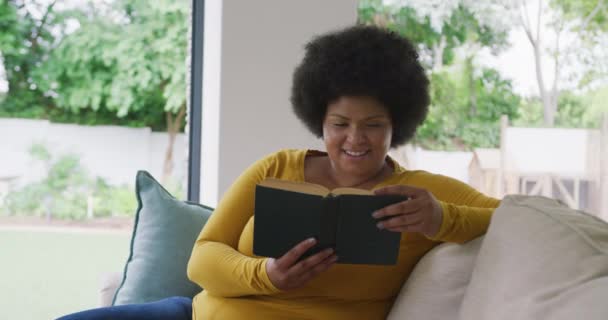 Видео Счастливой Плюс Размер Африканской Женщины Лежащей Диване Читающей Книгу — стоковое видео