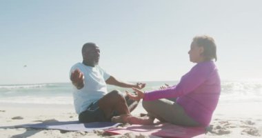 Kıdemli Afro-Amerikan çifti yoga yapıyor ve güneşli sahilde meditasyon yapıyor. sağlıklı, aktif emeklilik plaj tatili.