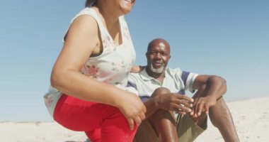 Gülümseyen kıdemli Afro-Amerikan çifti güneşli sahilde kucaklaşıp denize bakıyor. sağlıklı, aktif emeklilik plaj tatili.