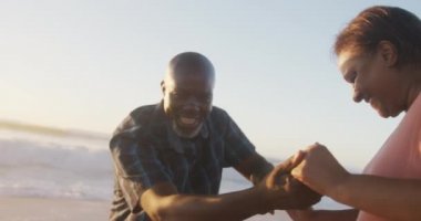 Gülümseyen son sınıf Afro-Amerikan çifti güneşli sahilde el ele tutuşup dans ediyorlar. sağlıklı, aktif emeklilik plaj tatili.