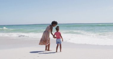 Güneşli sahilde kızıyla yürüyen gülümseyen Afro-Amerikan annesi. sağlıklı, aktif aile plaj tatili.