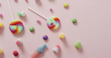 Pembe arka planda rengarenk tatlıların videosu. Renkli yemek, şeker, abur cubur ve tatlı konsepti.