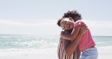 Güneşli plajda kızıyla kucaklaşan gülümseyen Afro-Amerikan annesi. sağlıklı, aktif aile plaj tatili.