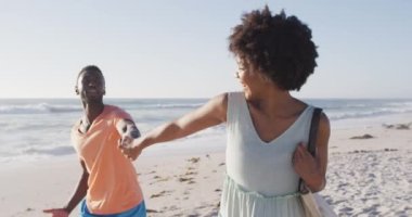 Gülümseyen Afro-Amerikan çifti el ele tutuşup güneşli sahilde yürüyor. sağlıklı, aktif aile plaj tatili.