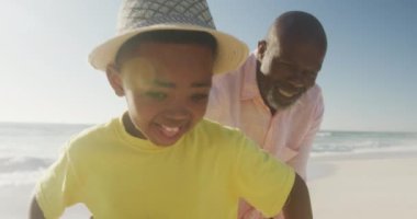 Güneşli sahilde torunuyla oynayan kıdemli Afro-Amerikan bir adam. sağlıklı, aktif emeklilik plaj tatili.