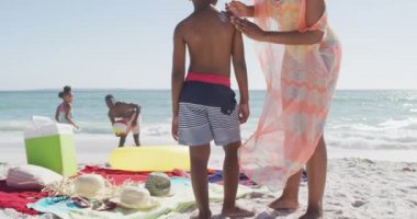 Gülümseyen Afro-Amerikan ailesi güneşli sahilde güneş kremi kullanıyor. sağlıklı, aktif aile plaj tatili.