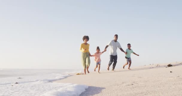 アフリカ系アメリカ人の家族が歩き 日当たりの良いビーチで手をつないで笑っています 健康的で活動的な家族のビーチホリデー — ストック動画