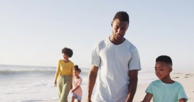 Gülümseyen Afro-Amerikan elele tutuşup güneşli sahilde yürüyor. sağlıklı, aktif aile plaj tatili.