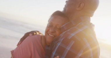 Gülümseyen kıdemli Afro-Amerikan çifti güneşli sahilde kucaklaşıyorlar. sağlıklı, aktif emeklilik plaj tatili.