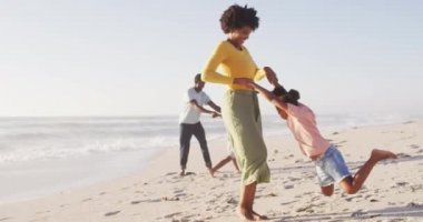 Gülümseyen Afro-Amerikan ailesi güneşli sahilde el ele tutuşup oynuyorlar. sağlıklı, aktif aile plaj tatili.