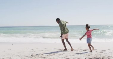 Gülümseyen Afrikalı Amerikalı baba ve kızı güneşli sahilde oynuyorlar. sağlıklı, aktif aile plaj tatili.