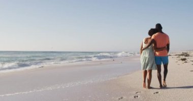 Afrika kökenli Amerikalı çift sarılıp güneşli sahilde yürüyorlar. sağlıklı, aktif aile plaj tatili.