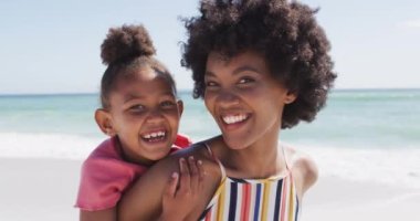 Güneşli sahilde gülümseyen Afrikalı Amerikalı anne ve kızının portresi. sağlıklı, aktif aile plaj tatili.