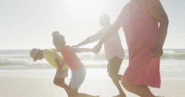 Gülümseyen son sınıf Afro-Amerikan çifti güneşli sahilde torunlarıyla koşuyor. sağlıklı, aktif emeklilik plaj tatili.