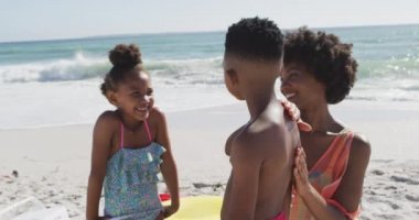 Gülümseyen Afro-Amerikan ailesi güneşli sahilde güneş kremi kullanıyor. sağlıklı, aktif aile plaj tatili.