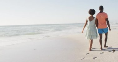 Afrika kökenli Amerikalı çift el ele tutuşup güneşli sahilde yürüyor. sağlıklı, aktif aile plaj tatili.