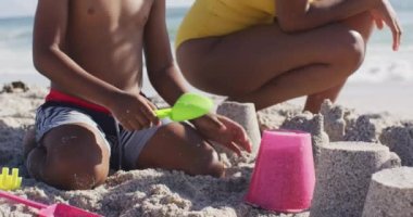 Güneşli sahilde kumdan kale inşa eden annesiyle gülümseyen Afro-Amerikan oğlu. sağlıklı, aktif aile plaj tatili.