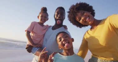 Güneşli sahilde kameraya bakan gülümseyen Afro-Amerikan aile portresi. sağlıklı, aktif aile plaj tatili.