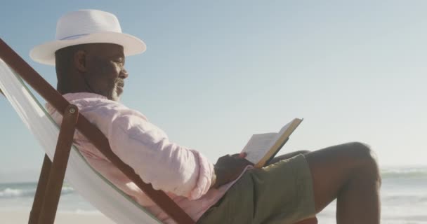 Χαμογελώντας Ηλικιωμένος Αφροαμερικάνος Ξαπλωμένος Στην Ξαπλώστρα Και Διαβάζοντας Βιβλία Στην — Αρχείο Βίντεο