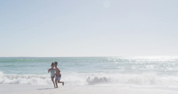 アフリカ系アメリカ人の兄弟の笑顔が晴れビーチで水着を着て走ります 健康的で活動的な家族のビーチホリデー — ストック動画