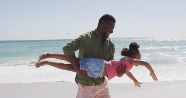 晴れたビーチで遊んでいる娘とアフリカ系アメリカ人の父親を笑顔 健康的で活動的な家族のビーチホリデー — ストック動画