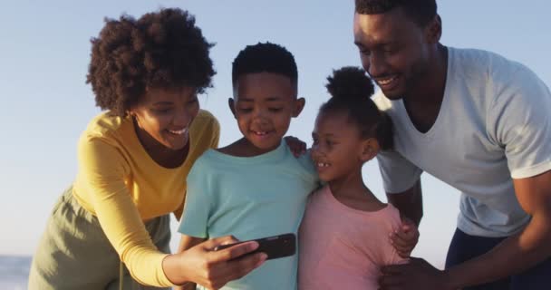 Smiling African American Family Using Smartphone Embracing Sunny Beach Healthy — Stock video