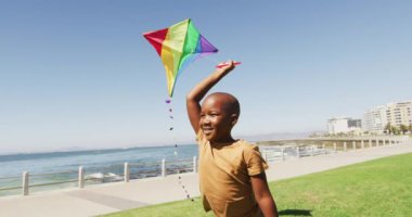 Mutlu Afrikalı Amerikalı bir çocuğun uçurtmayla eğlendiği, plajda koştuğu bir video. Aile, birliktelik, birlikte dışarıda kaliteli zaman geçirmek..