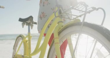 Gülümseyen son sınıf Afro-Amerikan çifti güneşli sahilde bisikletleriyle yürüyor. sağlıklı, aktif emeklilik plaj tatili.