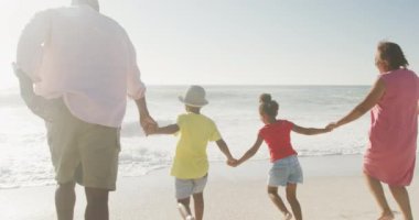 Gülümseyen son sınıf Afro-Amerikan çifti güneşli sahilde torunlarıyla koşuyor. sağlıklı, aktif emeklilik plaj tatili.