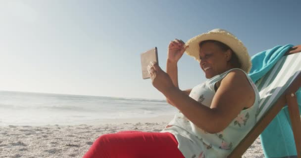 微笑着年长的非洲裔美国女人躺在日光浴床上 在阳光灿烂的海滩上看书 积极的退休海滩假期 — 图库视频影像