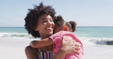 Güneşli plajda kızıyla kucaklaşan gülümseyen Afro-Amerikan annesi. sağlıklı, aktif aile plaj tatili.