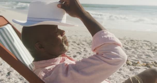 シニアアフリカ系アメリカ人の男性は日当たりの良いビーチで日なたぼっこをしている 健康的で活発な退職ビーチの休日 — ストック動画