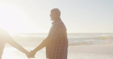 Gülümseyen son sınıf Afro-Amerikan çifti. El ele tutuşup güneşli sahilde yürüyorlar. sağlıklı, aktif emeklilik plaj tatili.