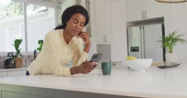 Afro-Amerikan kadının mutfakta akıllı telefon kullandığı bir video. ev ofisi ve online çalışma konsepti.