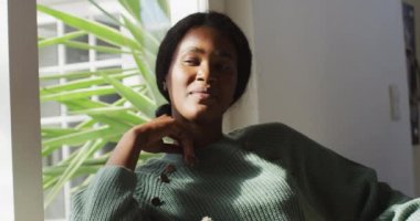 Video of relaxed african american woman looking outside window. lifestyle and spending free time at home.