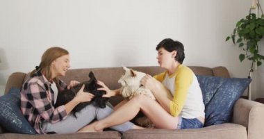 Kafkasyalı lezbiyen çift evdeki kanepede köpekleriyle oynuyorlar. lgbt ilişkisi ve yaşam tarzı konsepti
