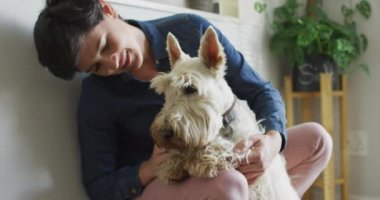 Beyaz bir kadın evdeki oturma odasında köpeğini öpüyor ve oynuyor. evcil hayvan sevgisi ve bakım kavramı